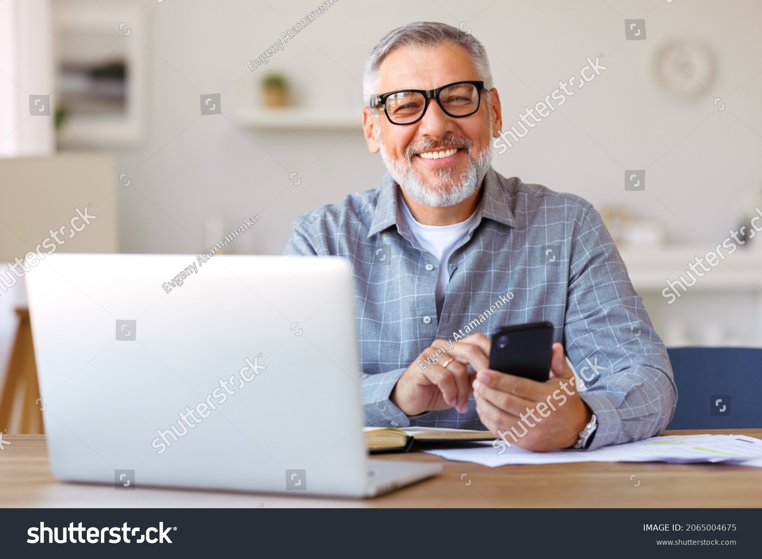 stock-photo-handsome-smiling-senior-man-wearing-glasses-using-mobile-phone-while-sitting-at-his-cozy-workplace-2065004675